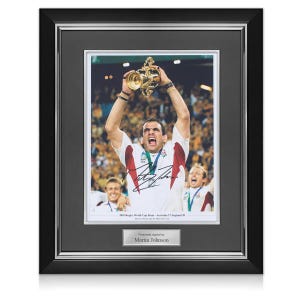 May include: A framed black and white photograph of a rugby player holding up a trophy. The player is wearing a white jersey with the number 17 on it. The photo is signed by Martin Johnson. The text below the photo reads "2003 Rugby World Cup Final - Australia 17 England 20.  Stadium Australia Sydney with the Webb Ellis Cup."