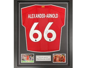 May include: A framed red soccer jersey with the name "Alexander-Arnold" and the number "66" on the back. The jersey is signed by Trent Alexander-Arnold. The frame includes two smaller photos of Alexander-Arnold playing soccer.