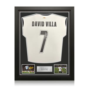 Può includere: Maglia da calcio bianca incorniciata con il nome "DAVID VILLA" e il numero "7" in nero. La maglia è firmata. Due piccole foto e una targa con la scritta "Firmato personalmente da David Villa" sono sotto. La cornice è nera.