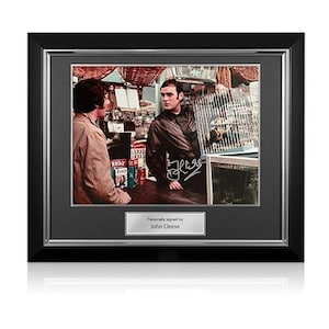 May include: Framed photograph featuring a scene with two men, one holding a birdcage. The image is signed and includes a plaque that reads "Personally signed by John Cleese." The frame is black with a silver border.