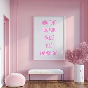 Könnte beinhalten: Ein weiß gerahmtes Bild mit rosa Text, der "I have to be successful because I like expensive shit" lautet, hängt an einer rosa Wand in einem Raum mit einer weißen Bank und einem rosa Hocker.