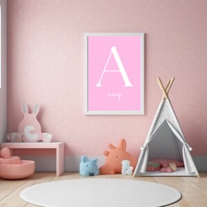 Può includere: Una cameretta rosa con una stampa incorniciata bianca con la lettera A e il nome Amy. La stanza ha una tenda a forma di tipi bianca, uno sgabello di legno rosa e una varietà di animali di peluche.