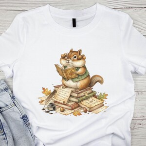 May include: A white t-shirt featuring a graphic of a chipmunk wearing glasses and a green vest, sitting on a stack of books while reading. The illustration includes scattered autumn leaves, a quill pen, an inkwell, and handwritten parchment.