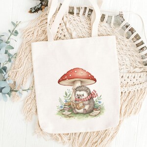 May include: A cream-colored tote bag featuring a whimsical illustration of a hedgehog reading under a red-capped mushroom. The hedgehog wears a scarf and glasses, surrounded by books and greenery. The bag has sturdy handles.