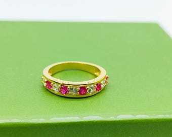 May include: A gold ring with alternating red and clear gemstones. The ring is set on a green surface. The gemstones are evenly spaced around the band.