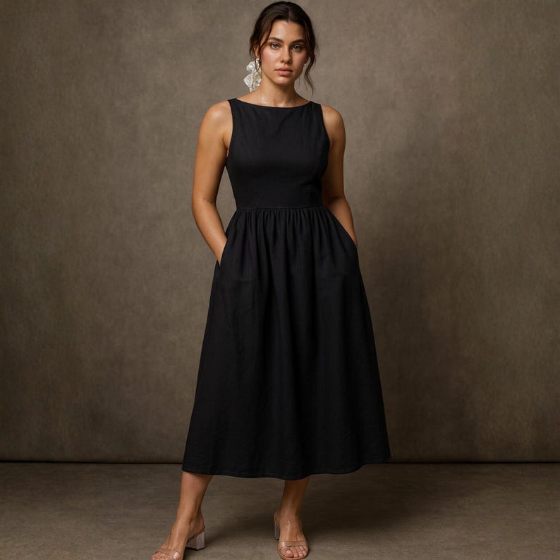 May include: A sleeveless black dress with a boat neckline and a gathered waist. The dress has pockets and falls to mid-calf. The model is wearing clear heels and earrings. The background is a solid brown.