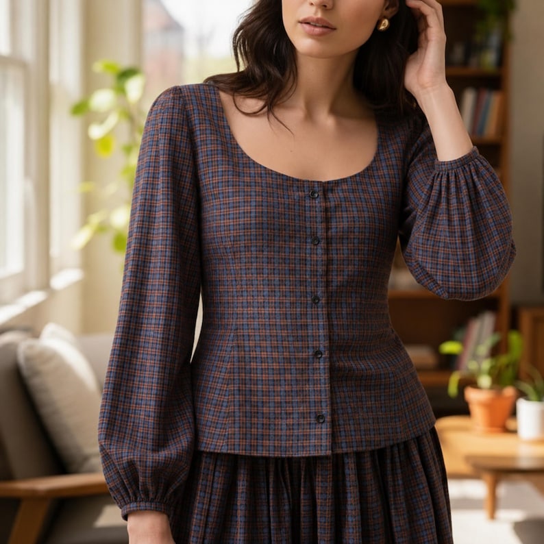 May include: A brown, blue, and orange plaid blouse with a scoop neckline and long, gathered sleeves. The blouse has a button-down front and is paired with a matching skirt. The outfit is a classic, vintage-inspired style.