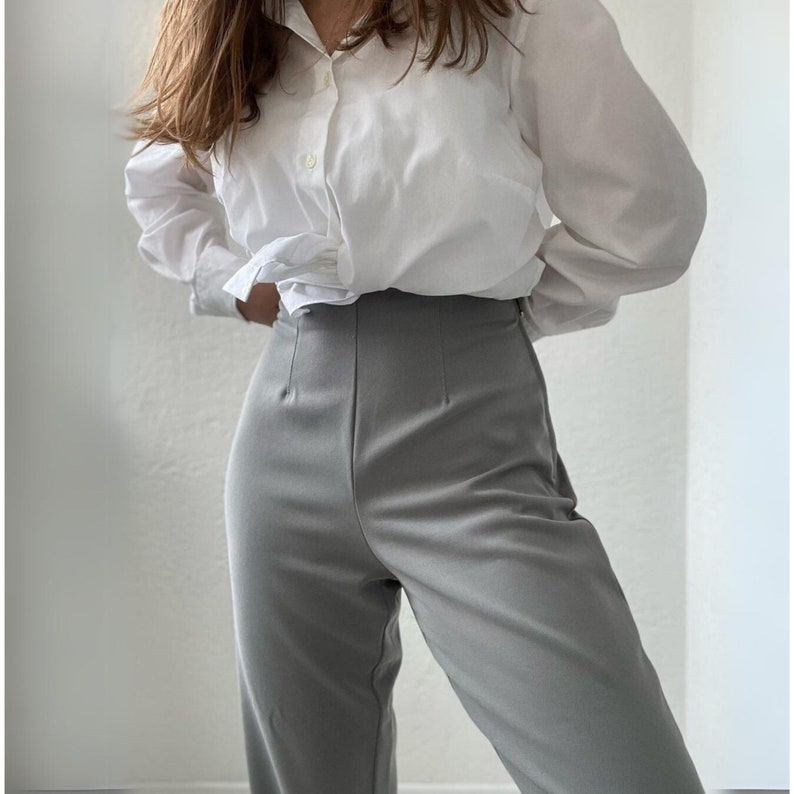 May include: A white button-down shirt with long sleeves and a gray pair of high-waisted pants.