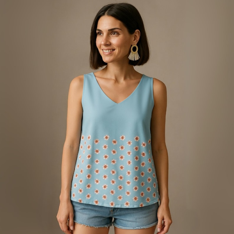 May include: A sleeveless, light blue top with a V-neck. The bottom half of the top features a repeating pattern of small white flowers with orange centers. The top is paired with denim shorts.