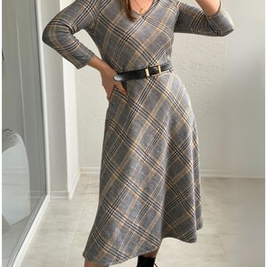May include: A gray and yellow plaid midi dress with a v-neck and 3/4 sleeves. The dress has a black belt with a gold buckle.