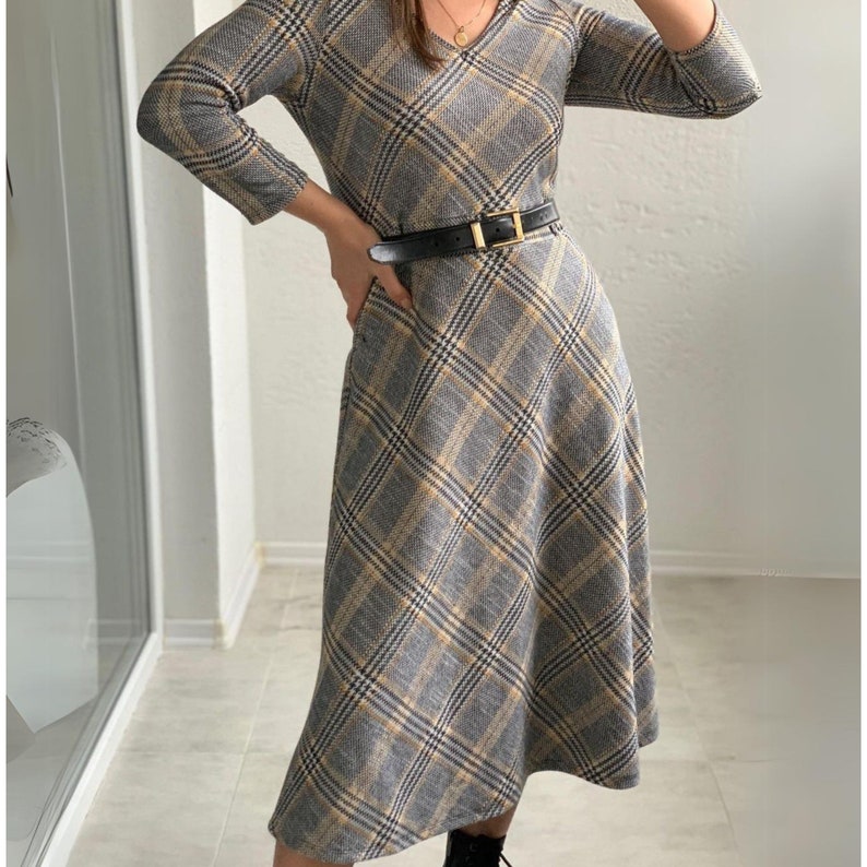May include: A gray and yellow plaid midi dress with a v-neck and 3/4 sleeves. The dress has a black belt with a gold buckle.