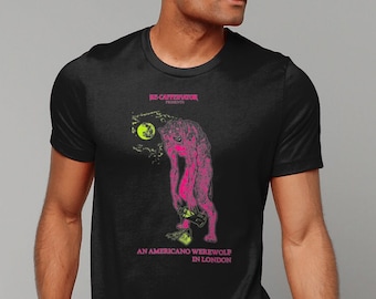 May include: A black t-shirt featuring a graphic print of a pink werewolf with a green moon in the background. The text "RE-CATHOLICIZE" and "AN AMERICANO WEREWOLF IN LONDON" is printed on the shirt.
