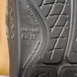 May include: Close-up of the sole of a black shoe. The sole has a textured pattern with diamond shapes and cross-shaped grooves. The size is marked as 144-W9, EU 37.