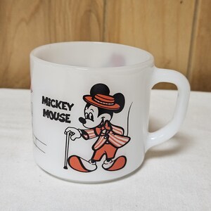 Pu&ograve; includere: Tazza in ceramica bianca con Topolino in un completo rosso e arancione con un bastone. La tazza ha un manico curvo e le parole "Mickey Mouse" stampate sul lato. Il design &egrave; in stile vintage.