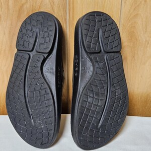 May include: A pair of black sandals, viewed from the soles. The sandals have a textured, patterned design on the soles. The sandals are made of a solid, dark material. The sandals are EU size 37.