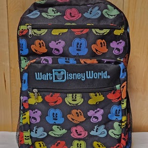 Puede incluir: Una mochila negra con un patr&oacute;n repetitivo de siluetas de cabezas de Mickey Mouse coloridas en rosa, verde, azul, naranja y amarillo. El frente incluye un bolsillo con cremallera con el texto bordado Walt Disney World en azul claro.