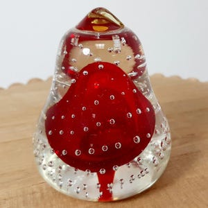 May include: A clear glass paperweight with a red core and a golden top. The red core has a pear shape and is filled with small air bubbles. The clear glass exterior also has air bubbles.