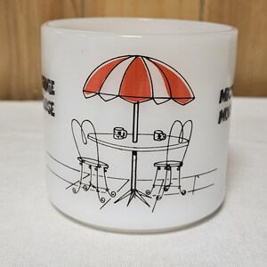 Pu&ograve; includere: Tazza in ceramica bianca con grafica nera e rossa di una scena di caff&egrave;. Il design include un ombrellone a strisce rosse e bianche, un tavolo, due sedie e le parole "Mickey Mouse" sul lato.