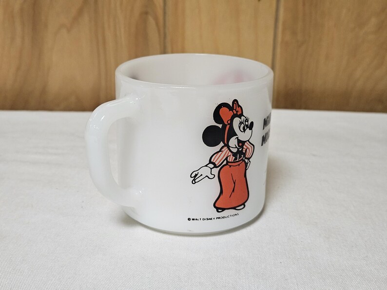 Pu&ograve; includere: Tazza in ceramica bianca con un design a cartoni animati di Minnie Mouse. Minnie &egrave; raffigurata con un vestito e un fiocco rossi, con una camicia a righe. La tazza ha un manico curvo e il testo "Minnie Mouse". Un oggetto da collezione Disney vintage.