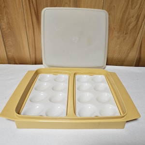 May include: A rectangular, light yellow plastic egg storage container with two removable white trays, each featuring eight oval-shaped indentations. The set includes a matching light yellow base and a separate, flat, translucent off-white lid.