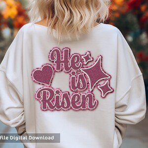 May include: White sweatshirt with a pink glitter design that says "He is Risen" with a heart and star accents.