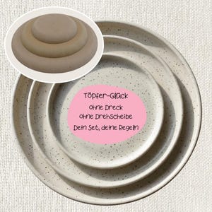 Könnte beinhalten: Ein Set aus drei gesprenkelten Keramikplatten in verschiedenen Größen, mit einem kleinen, kreisförmigen, hellfarbigen Objekt in der oberen linken Ecke. Die Platten haben eine neutrale Farbe mit dunklen Sprenkeln. Text auf einem rosa Oval: Töpfer-Glück...