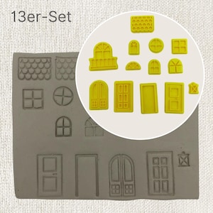 Könnte beinhalten: Ein Set mit 13 gelben Silikonformen zum Herstellen von Fondant- oder Gummipaste-Dekorationen. Die Formen zeigen verschiedene Formen von Fenstern und Türen, darunter gewölbte, rechteckige und runde Designs. Die Formen sind auf einer grauen Silikonmatte angeordnet, auf der der Text "13er-Set" in Schwarz gedruckt ist.