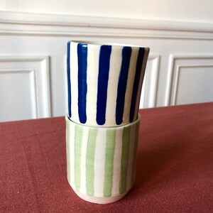 May include: Two ceramic mugs stacked on top of each other. The top mug has blue and white stripes, and the bottom mug has green and white stripes.