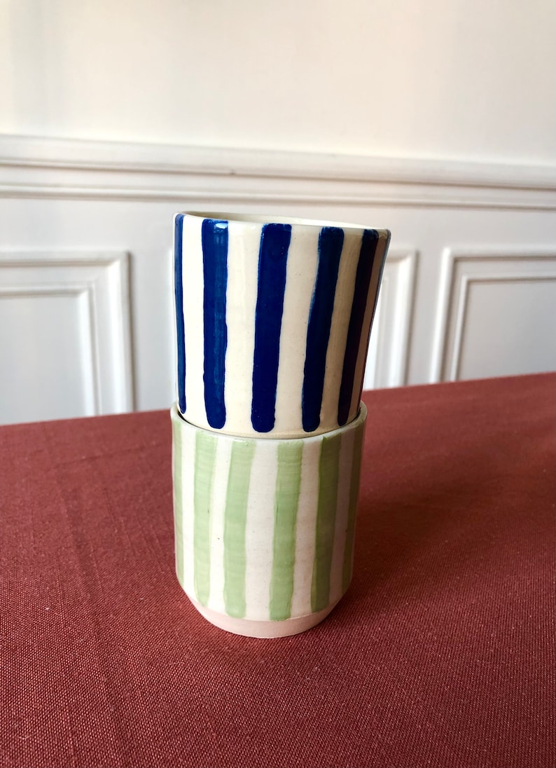 May include: Two ceramic mugs stacked on top of each other. The top mug has blue and white stripes, and the bottom mug has green and white stripes.