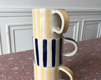 May include: Three ceramic mugs stacked on top of each other. The mugs are white with yellow and blue stripes.