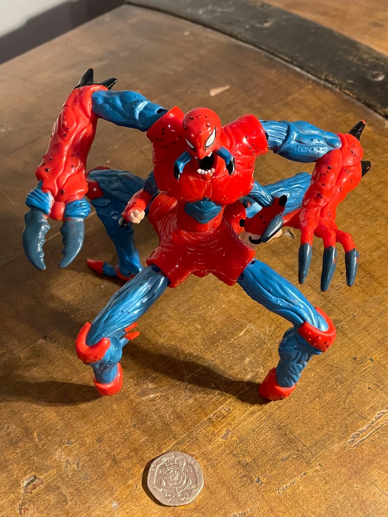 K&ouml;nnte beinhalten: Eine rote und blaue Actionfigur von Spider-Man mit mehreren Beinen und Krallen. Die Figur ist in einer bedrohlichen Pose mit offenem Mund und sichtbaren Z&auml;hnen dargestellt.