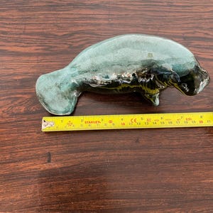 Peut inclure: Une figurine de lamantin en céramique verte avec un glaçage blanc et jaune. La figurine mesure environ 18 cm de long.