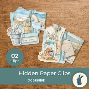 Op de afbeelding: Twee decoratieve paperclips met illustraties in strandthema. De ene clip toont een emmer gevuld met schelpen en de tekst Beach, Please. De andere clip toont een glazen pot met schelpen, een zandkasteel en de tekst you were here.