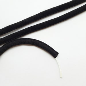 Könnte beinhalten: Schwarzes Gummiband mit einer weißen Plastikspitze. Das Band ist in der Mitte gefaltet und die Spitze ist am Ende sichtbar.