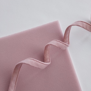 Könnte beinhalten: Nahaufnahme eines hellrosa Stoffes mit einem rosa Band, das darauf gelegt ist. Das Band ist wellenförmig gefaltet.