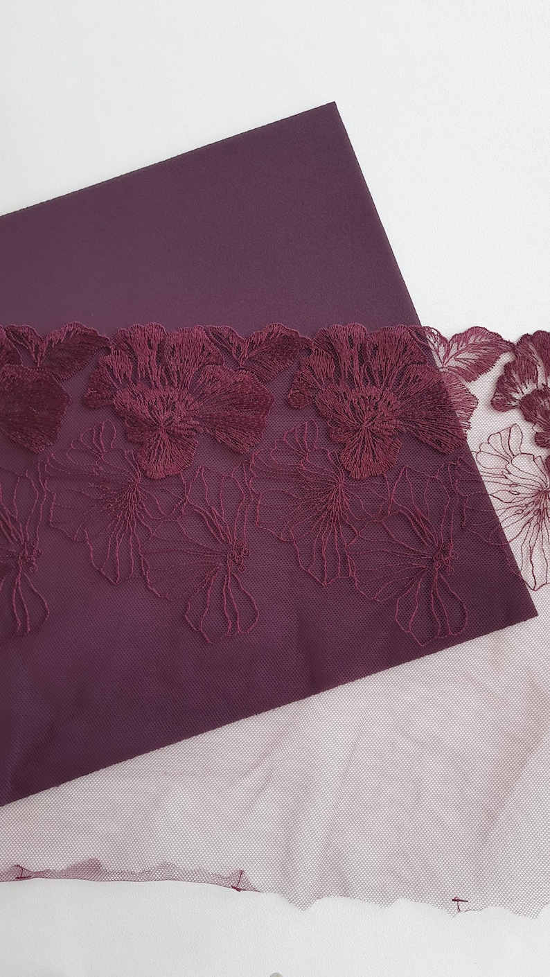 May include: Burgundy fabric with a burgundy floral lace trim. The lace is delicate and has a floral pattern.