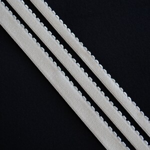 May include: Three white elastic bands with scalloped edges on a black background.