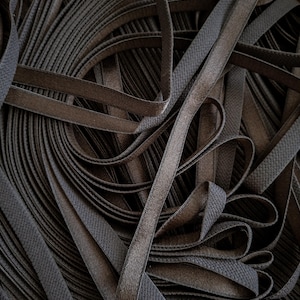 Peut inclure: Gros plan sur un tas de bandes élastiques marron foncé. Les bandes sont superposées et entrelacées, créant un motif texturé. L'élastique semble être fait d'un matériau tissé.