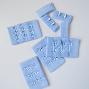 Puede incluir: Un juego de siete extensores de tirantes de sujetador de color azul claro con ganchos blancos. Los extensores están hechos de un tejido suave y elástico y tienen múltiples cierres de gancho y ojo.