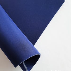 Puede incluir: Primer plano de una tela azul oscuro, enrollada para mostrar la textura del material. La tela está etiquetada como "azul oscuro".