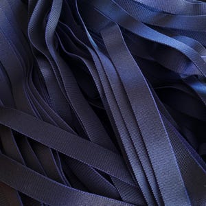 May include: Close-up of a pile of navy blue ribbon. The ribbons are made of a smooth, woven material and are layered on top of each other. The ribbons are of varying lengths and widths, creating a textured effect.