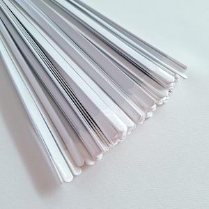 Può includere: Primo piano di una pila di oggetti bianchi, piatti e rettangolari. Gli oggetti sono disposti a ventaglio, con bordi leggermente arrotondati. Sembrano essere fatti di un materiale liscio e lucido.