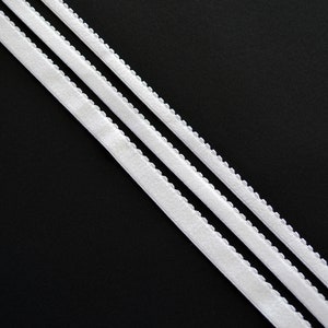 May include: Two white elastic bands with scalloped edges on a black background.