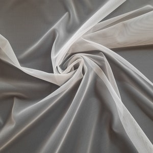 May include: White tulle fabric with a soft, delicate texture. The fabric is draped and folded, showcasing its sheer and airy quality.