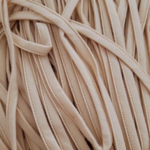 May include: Close-up of a pile of beige elastic trim. The trim is made of a soft, fabric material and has a stitched edge. The trim is used for sewing and crafting projects.