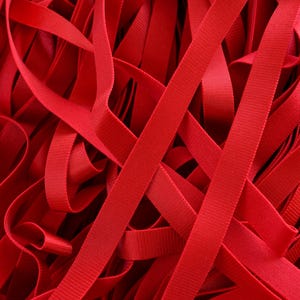 May include: Close-up of a pile of bright red ribbon. The ribbons are layered and intertwined, creating a textured and visually engaging pattern. The ribbons appear to be made of a smooth, possibly satin-like material.