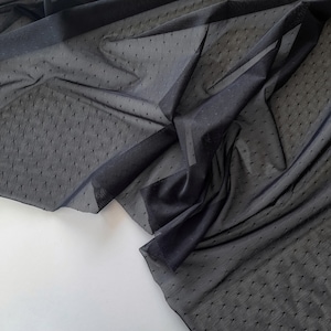 May include: Dark navy blue sheer fabric with a dotted pattern. The fabric is draped and folded, creating shadows and texture. The material appears lightweight and delicate, suitable for apparel or craft projects.