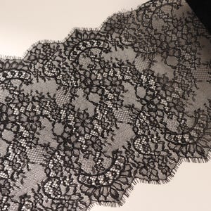 Puede incluir: Tela de encaje negro con un patrón floral y un borde festoneado. El delicado material está parcialmente enrollado, revelando el intrincado diseño. Adecuado para diversos proyectos de costura y manualidades.