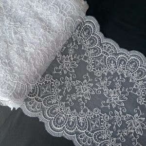 Puede incluir: Tela de encaje blanco con diseño floral y borde festoneado. El encaje está enrollado, mostrando los intrincados patrones y texturas. Los delicados detalles incluyen flores, hojas y formas geométricas, ideal para proyectos de manualidades y costura.
