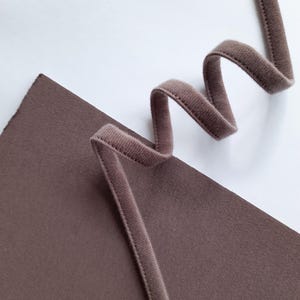 May include: A close-up of a brown elastic band with a slightly textured surface. The band is curled and folded on a brown surface.